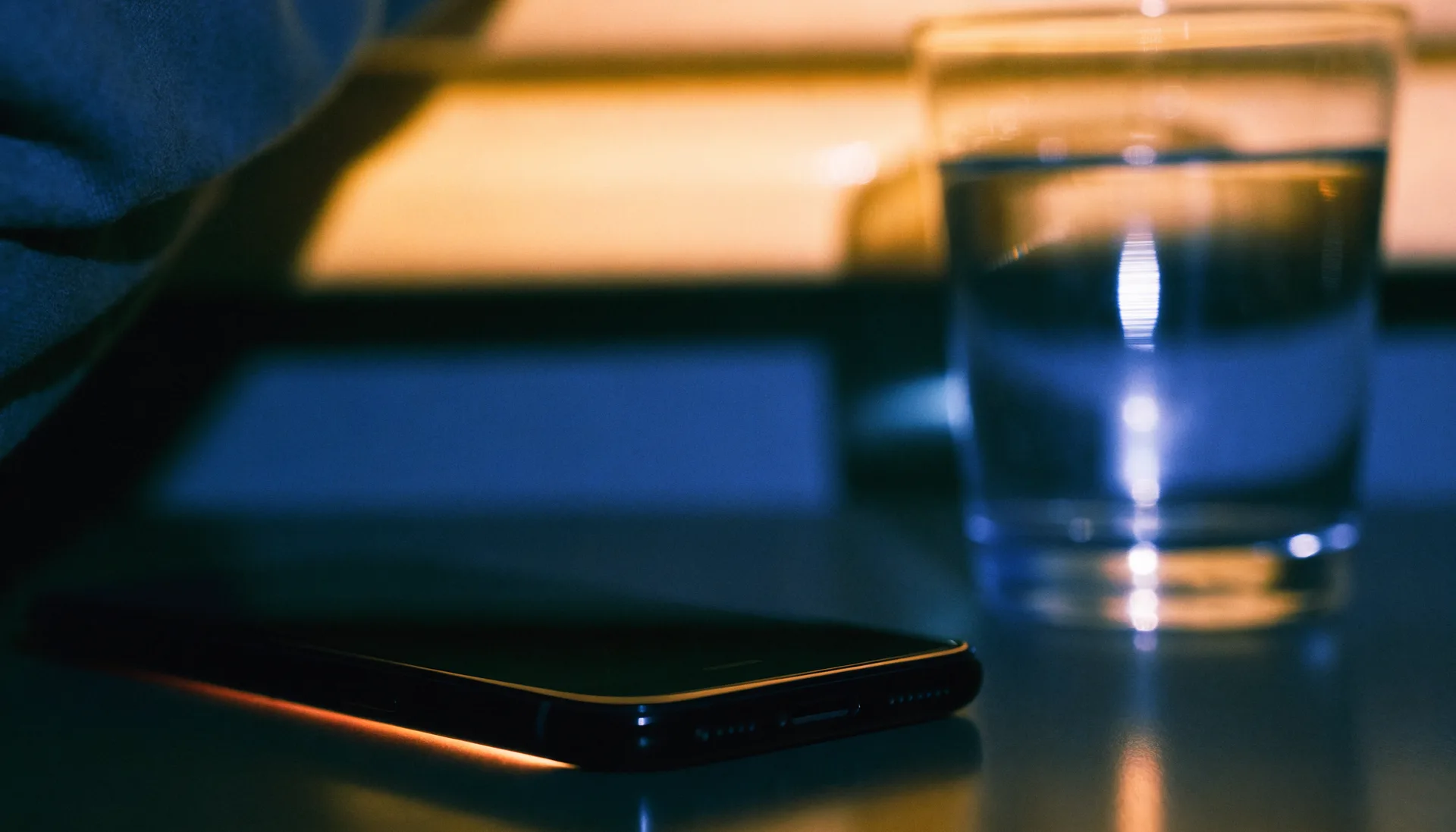 A phone lying face-down on a nightstand at two in the morning, a thin amber glow escaping around its edges.